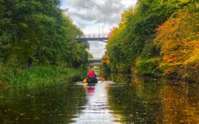 a kayak paddles along a canal towards a road bridge
