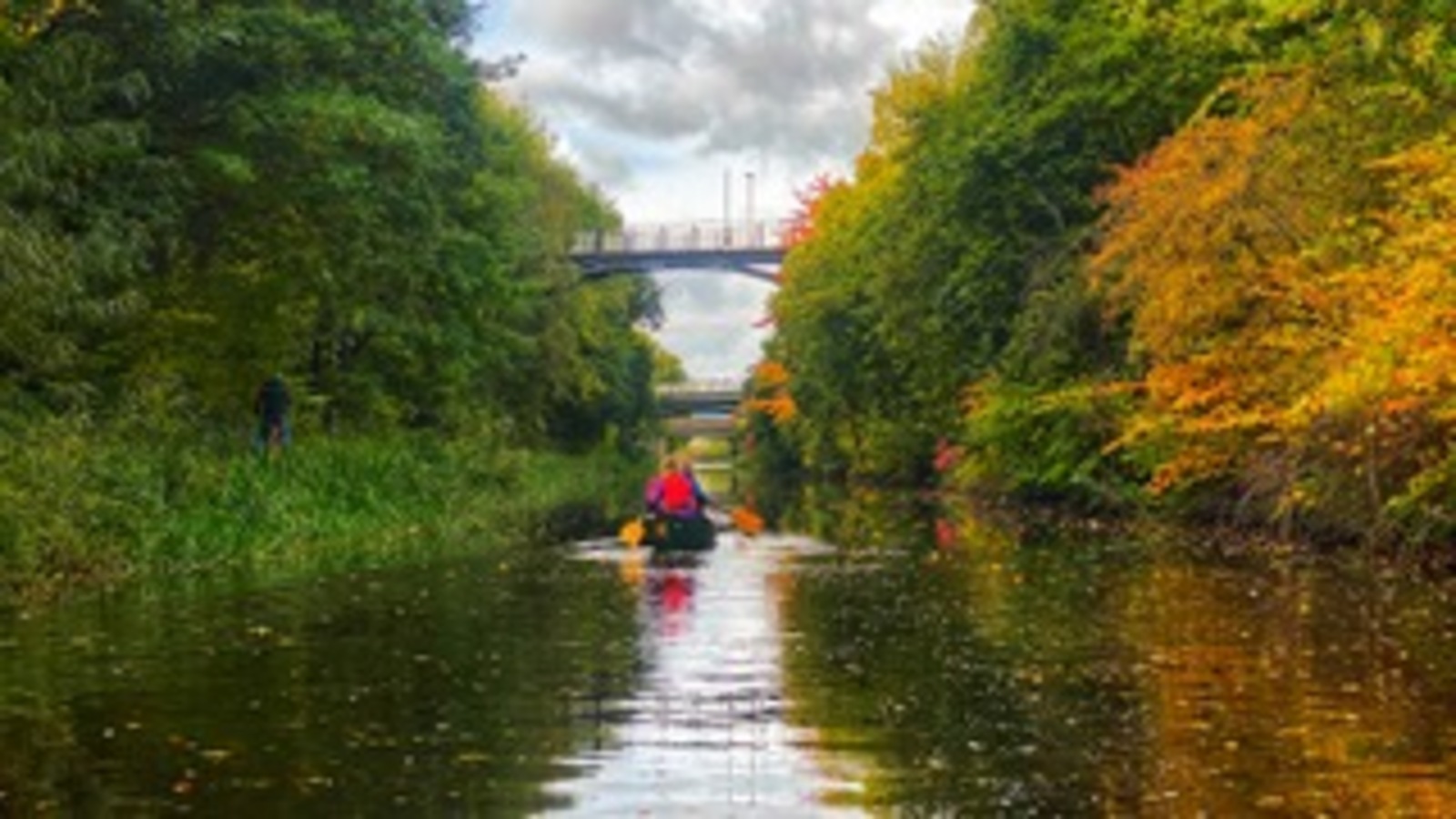 a kayak paddles along a canal towards a road bridge