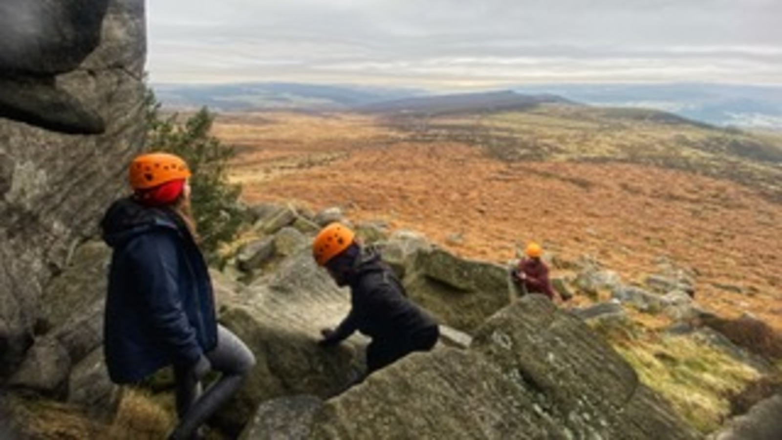 3 people scramble amongst gritstone boulders