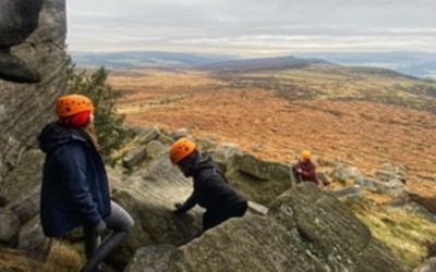 3 people scramble amongst gritstone boulders