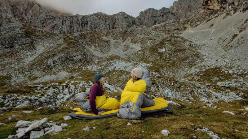 Two adventurers in Rab sleeping bags hanging out with each other infront of rockface 